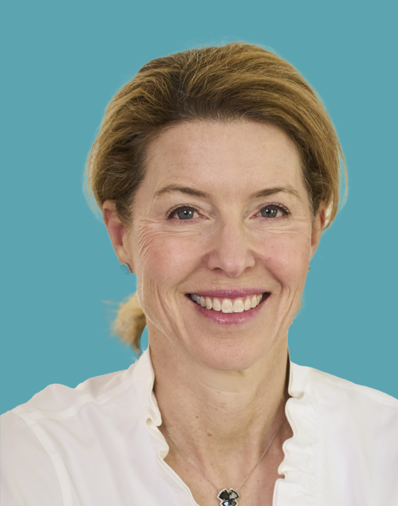 Smiling woman with light brown hair and a white blouse against a blue background.